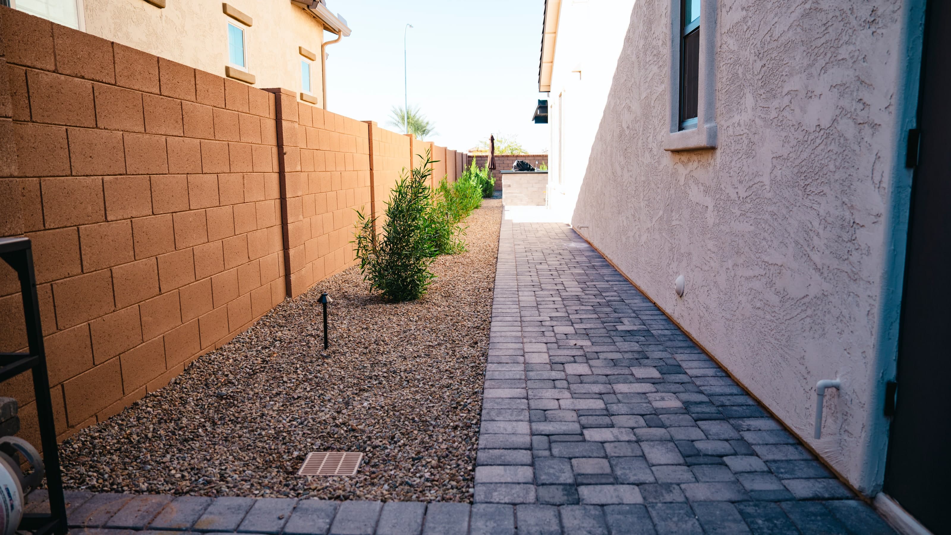 Paver side-yard path beside gravel planting, a drain grate, and a block wall at a new-build home in Chandler