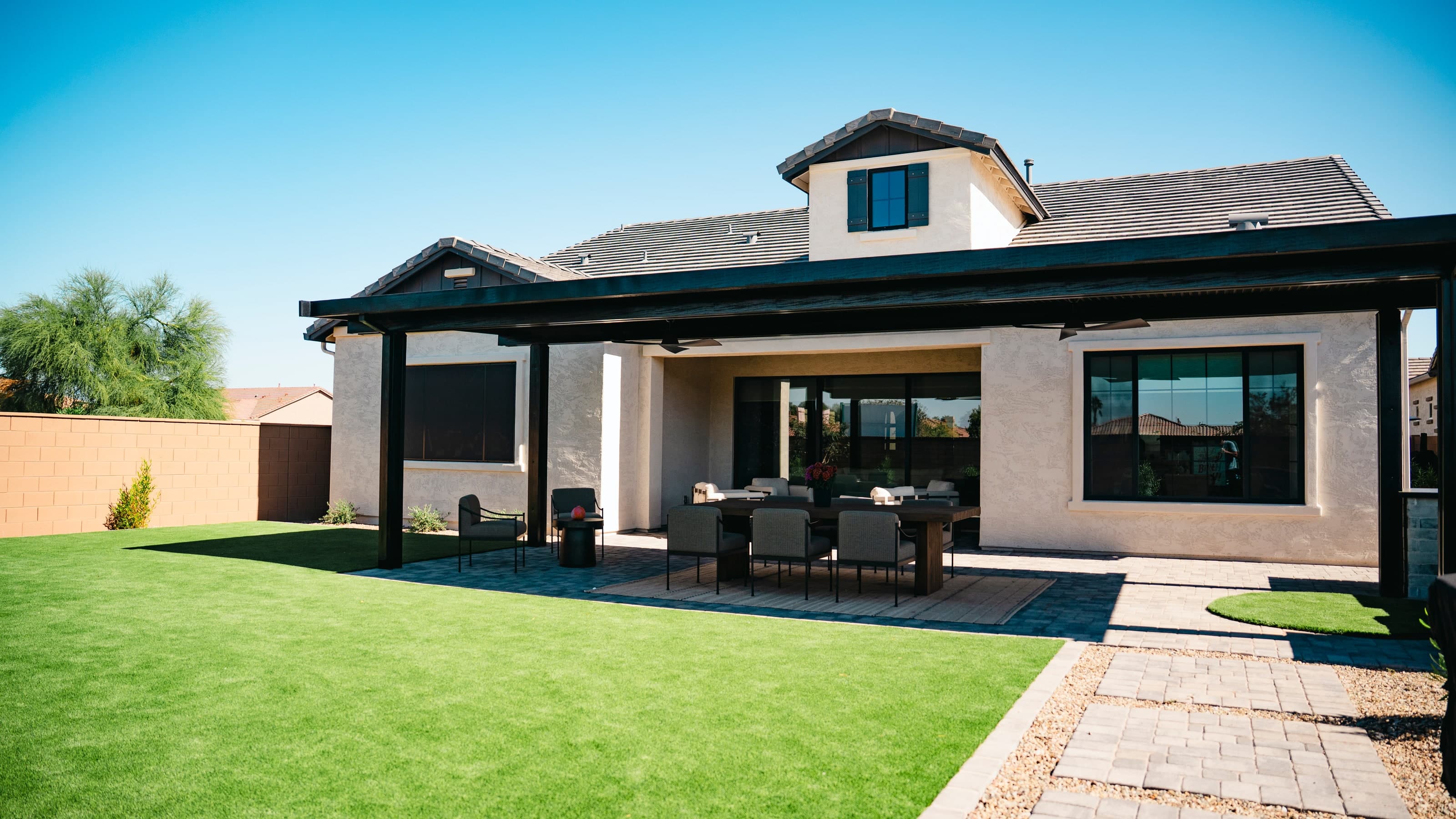 Rear elevation of a home with a large linear-slat shade structure over a dining area and turf backyard