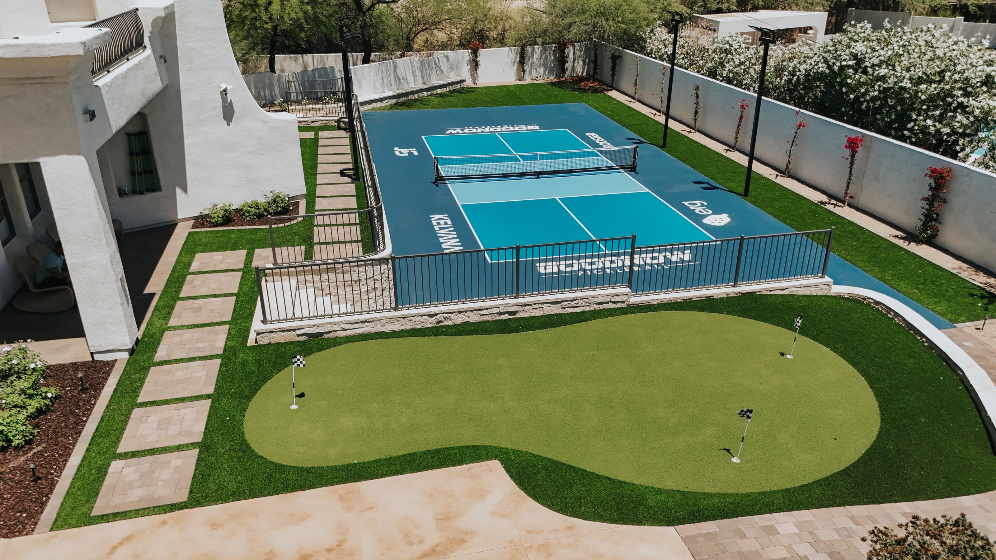 Aerial view of a backyard pickleball court with custom court graphics and a putting green beside a two-story home in Arcadia