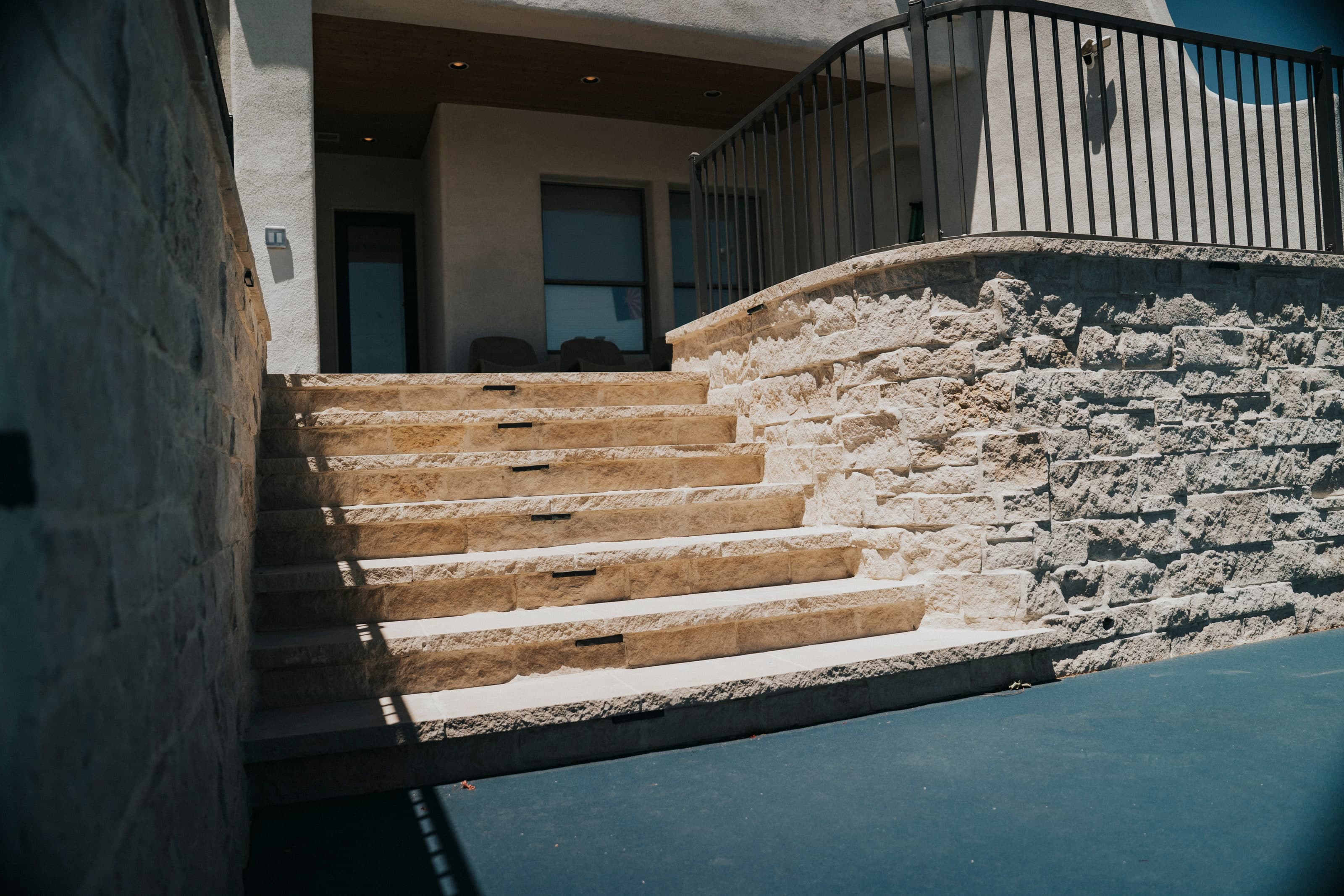 Stone steps set into a stacked-stone retaining wall, stepping down from the house to a sunken sport court in an Arcadia backyard