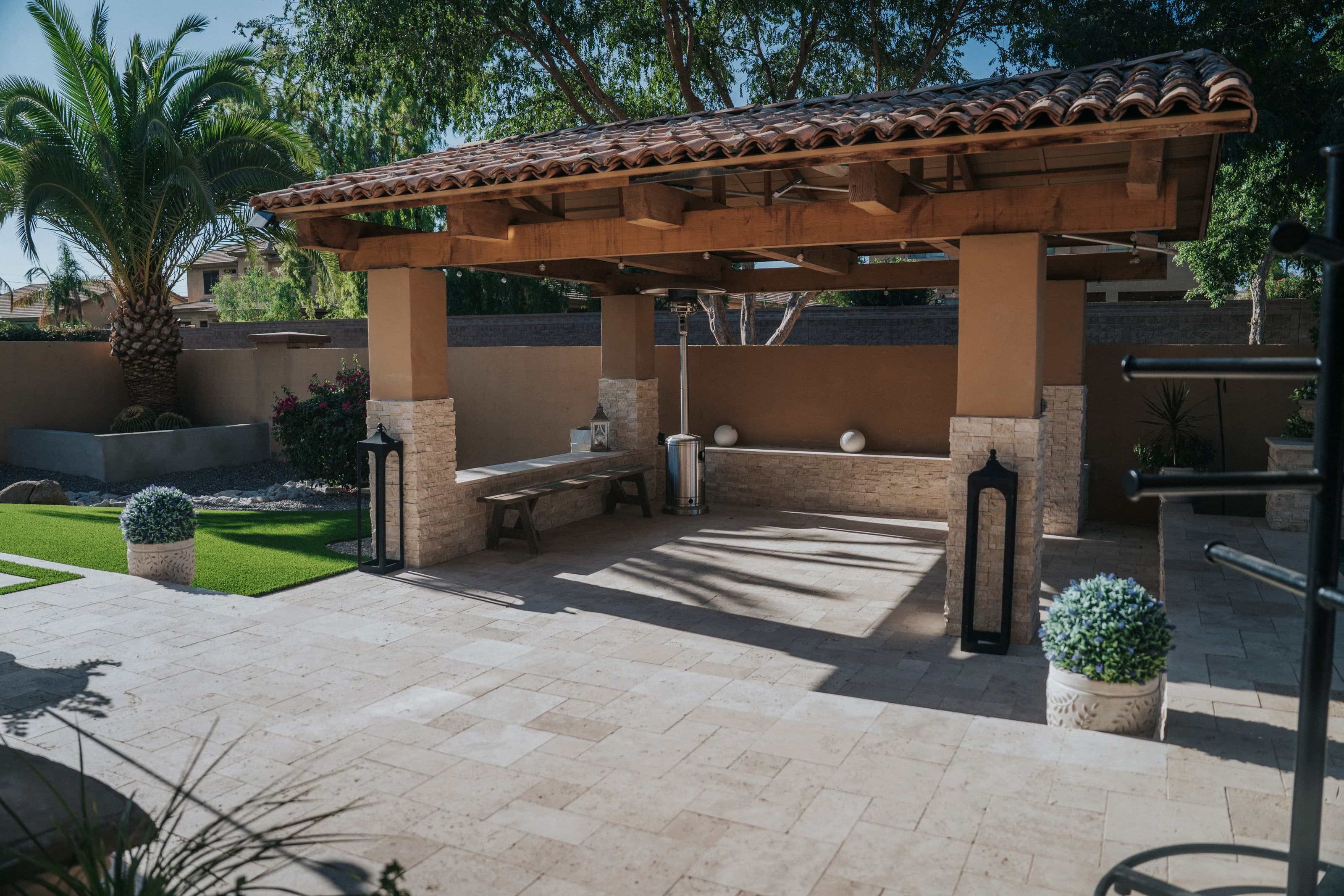 Wood-beam ramada with stacked-stone column bases on a travertine patio in a Chandler backyard