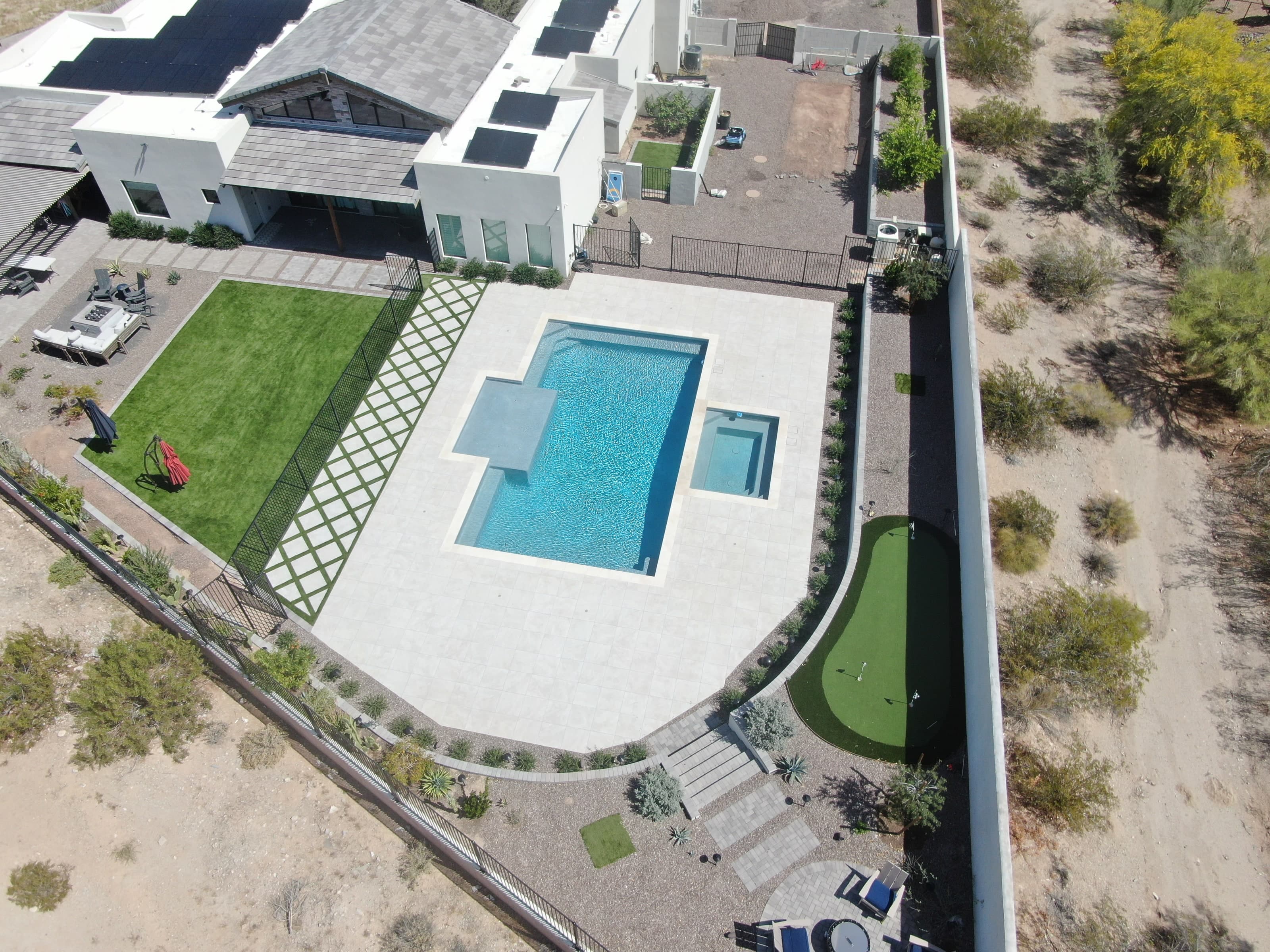 Aerial view of a finished Queen Creek backyard: a pool and spa with large-format decking, a turf lawn, the turf-and-paver diamond grid, a putting green, and a fire pit