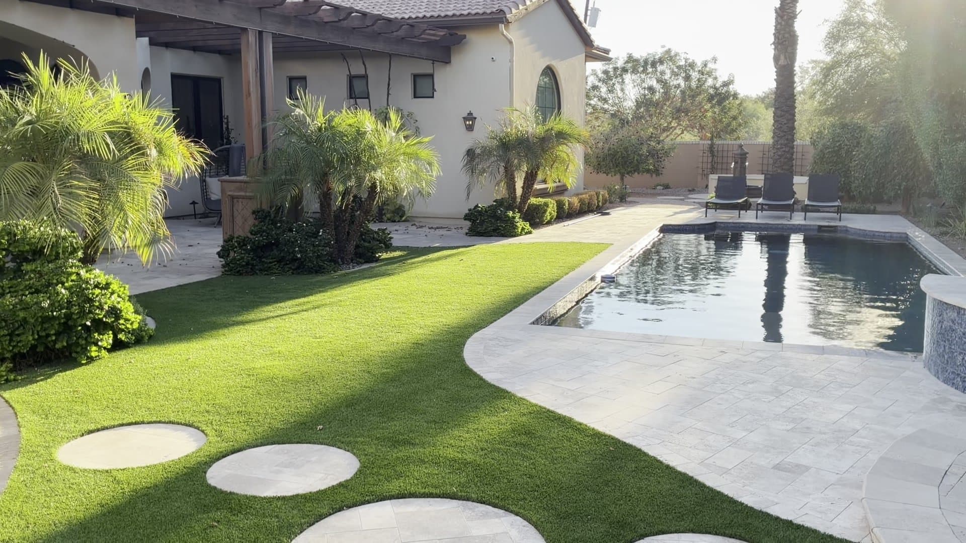 Circular travertine stepping pads crossing a turf lawn toward a rectangular pool, with palms and the house behind