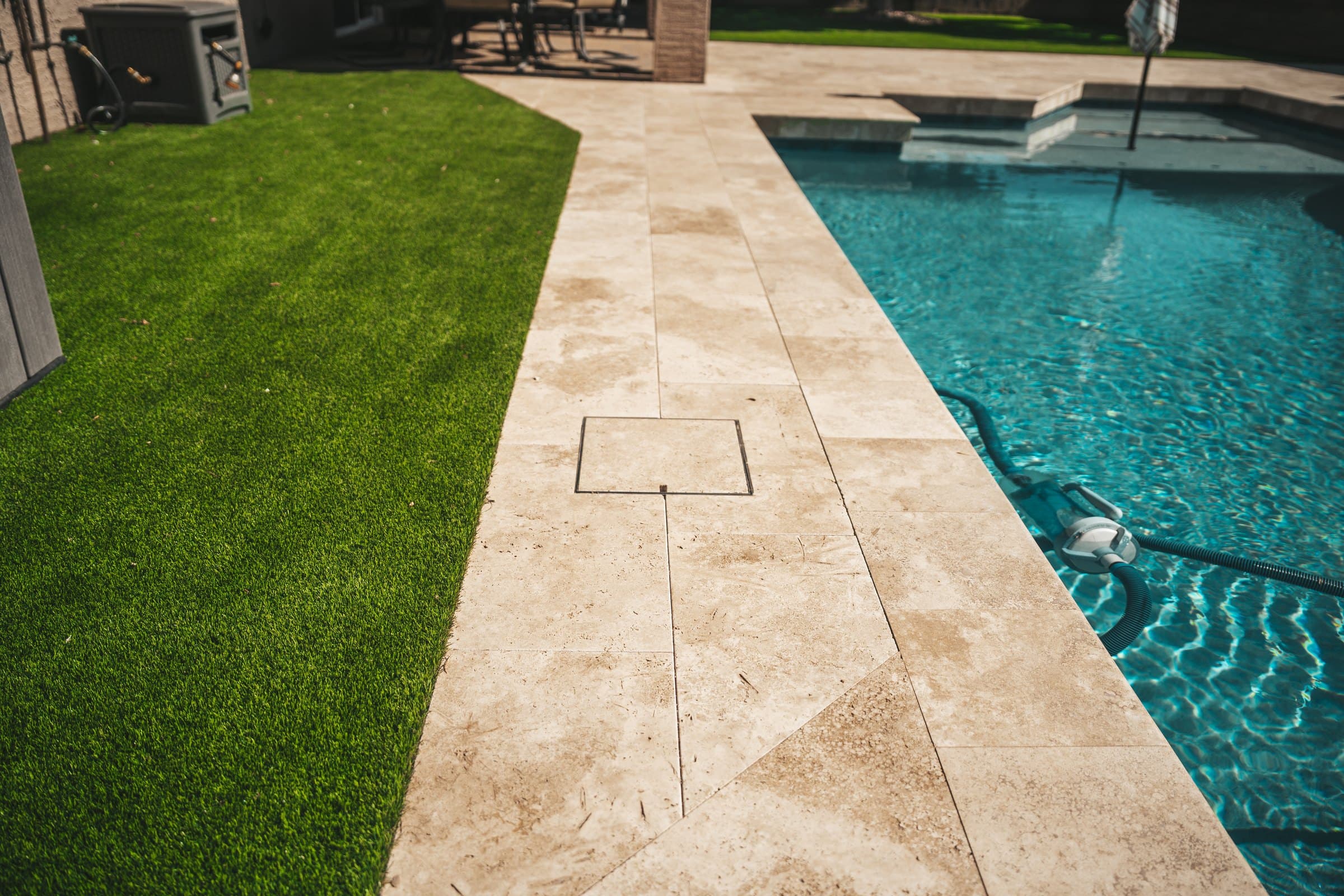 A strip of travertine decking running between a turf lawn and the pool, toward the back of the house