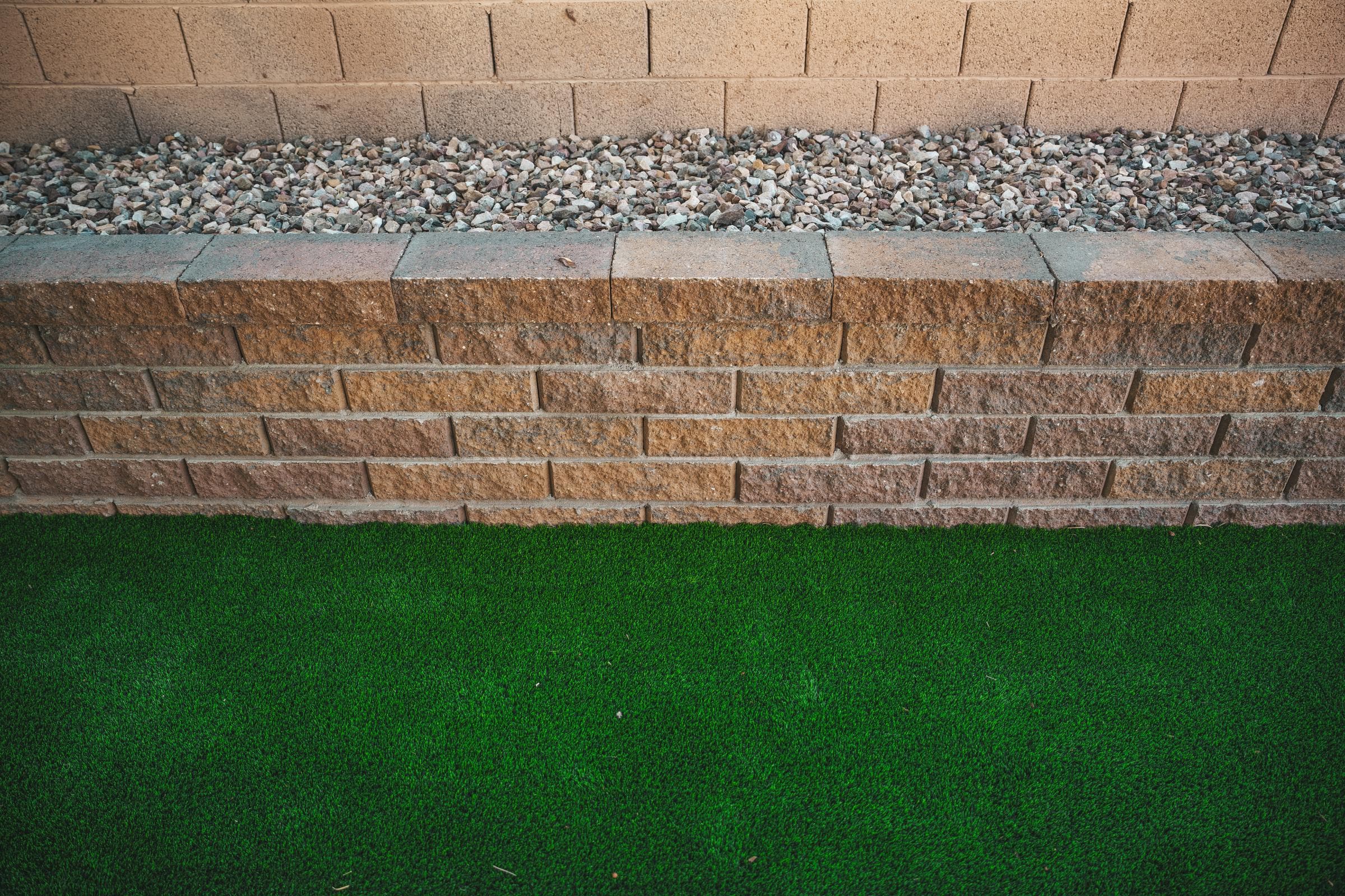 A capped block planter wall filled with gravel along a perimeter wall, with turf in front